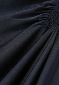 Mørk navy stof med en glat, satinlignende tekstur, der har samlet detaljer og flydende draperinger, som antyder elegant bevægelse.