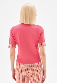 Kortärmad rosa stickad topp med mönstrade manschetter och fåll med röda och gula accenter, slät textur och figurnära design.