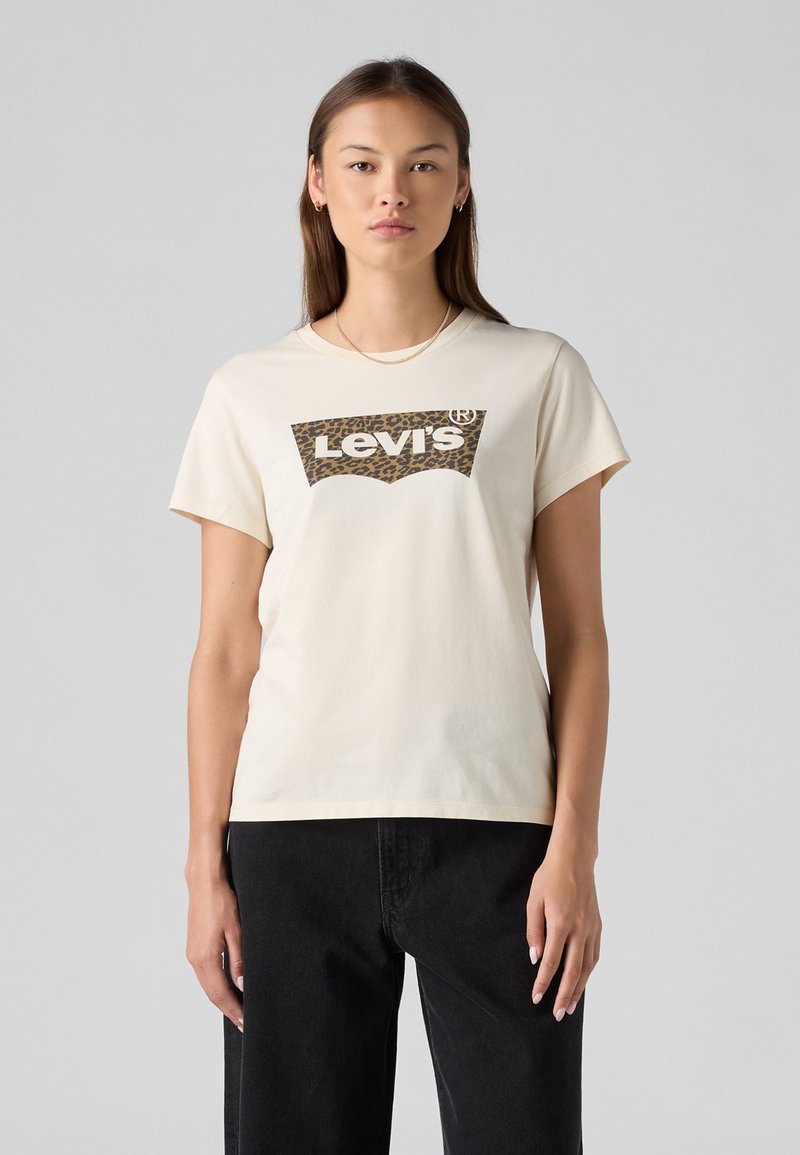 Kreminės spalvos trumpomis rankovėmis medvilninė marškinėliai su rudos spalvos leopardų raštą turinčiu Levi's logotipu priekyje. Derinami su juodais džinsais.