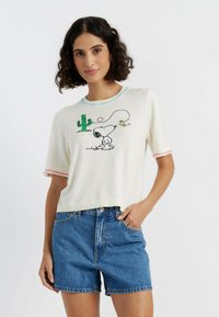 Witte gebreide kortekraag trui met korte mouwen, voorzien van een kleurrijk geborduurd Snoopy-ontwerp met een cactus en een ster, en contrasterende stiksels op de halslijn en mouwen.