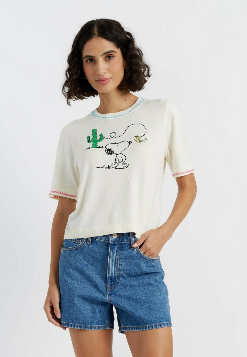 Witte gebreide kortekraag trui met korte mouwen, voorzien van een kleurrijk geborduurd Snoopy-ontwerp met een cactus en een ster, en contrasterende stiksels op de halslijn en mouwen.