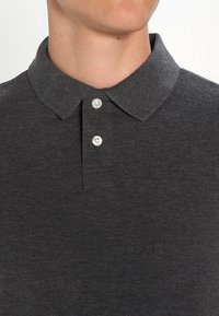 Polo shirt gris foncé avec un col rabattu, patte de boutonnage à trois boutons et un tissu texturé. Pas de motifs ni d'accents visibles.