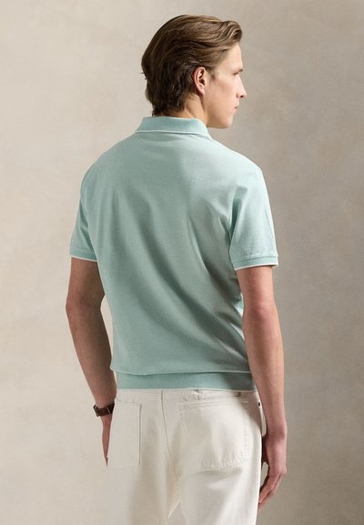 Πόλο μπλουζάκι σε χρώμα μέντας, κατασκευασμένο από υφασμάτινη υφή, με κοντά μανίκια και ριμπ γιακά. Συνδυάζεται με ανοιχτόχρωμο παντελόνι.