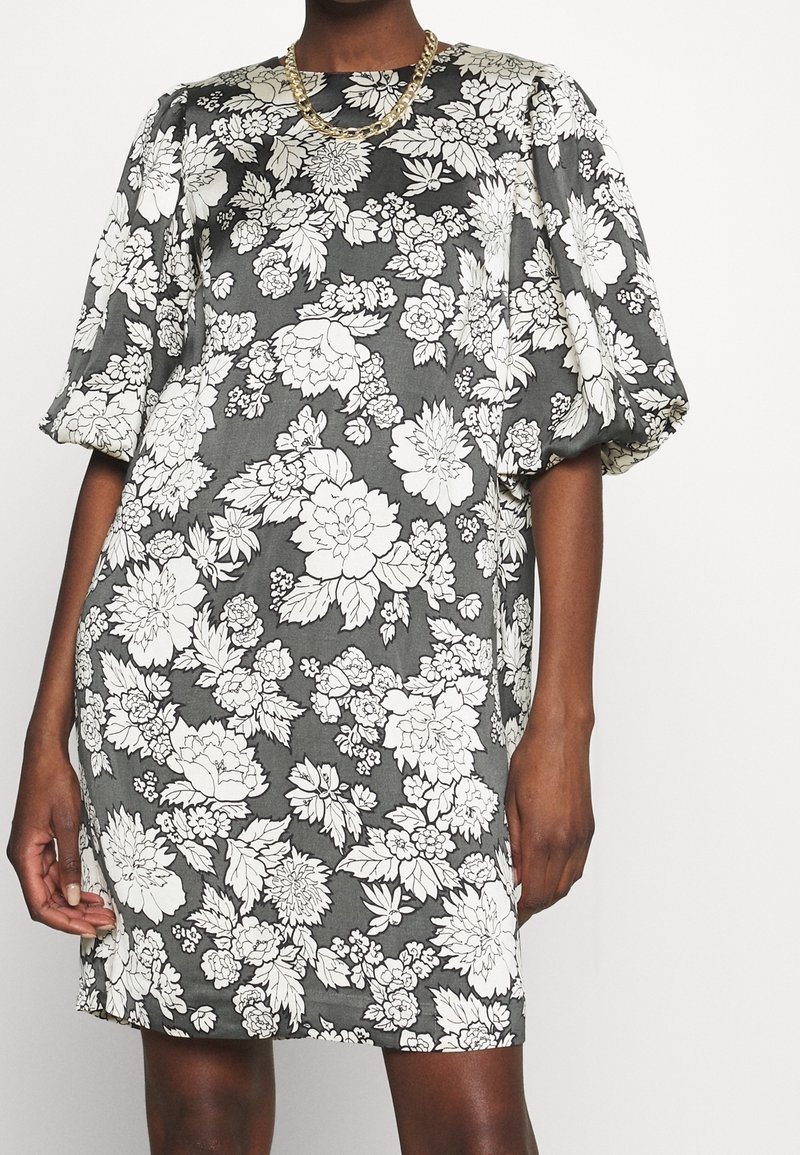 Sukienka w kwiaty wykonana z szarego materiału z białymi kwiatami. Posiada krótkie, bufiaste rękawy i prosty krój. Powierzchnia wydaje się gładka.