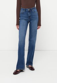 Jeans acampanados de cintura alta en mezclilla azul medio, con bolsillos frontales y un cierre de botón clásico. Textura suave y líneas limpias.