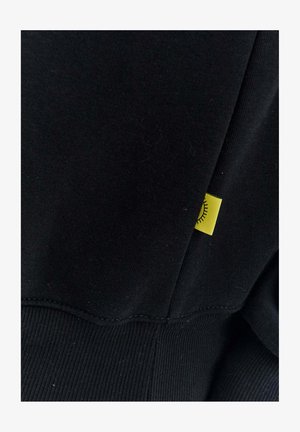 Čierna mikina vyrobená z látky s rebrovanou textúrou. Obsahuje malú žltú nášivku s dizajnom slnka prišitou na bočnom šve.