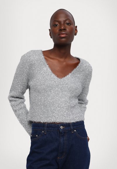 Sølv, pelsaktig genser med dyp V-hals og lange ermer, kombinert med indigo denimjeans med knappeåpning og subtile sømmer.
