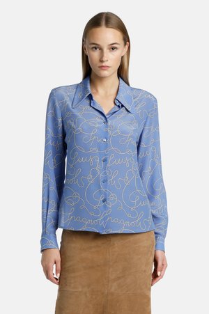 Blauwe zijden blouse met een kraag, voorzien van een cursief wit patroon. Lange mouwen en knoopsluiting aan de voorkant. Gladde textuur.