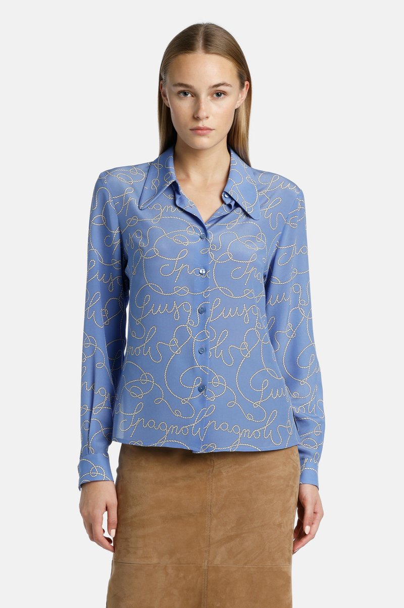 Blauwe zijden blouse met een kraag, voorzien van een cursief wit patroon. Lange mouwen en knoopsluiting aan de voorkant. Gladde textuur.