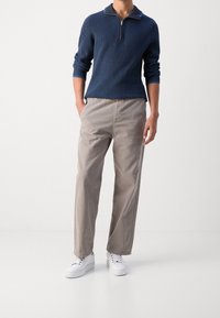 Maglione a collo con zip in maglia blu navy, maniche lunghe, abbinato a pantaloni grigio chiaro e dalla vestibilità ampia e sneakers bianche. Tessuto liscio e vestibilità casual.