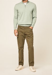 Jasnozielony sweter na zamek, długie rękawy, w połączeniu z khakimi spodniami. Białe sportowe buty dopełniają strój. Prosty, casualowy design.