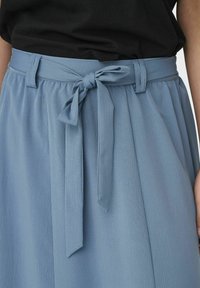 Jupe bleu clair en tissu texturé avec une ceinture à nouer à la taille. Présente des plis et un design de ceinture lisse.