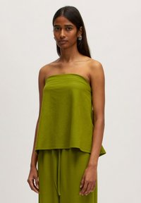 Grüntop ohne Träger aus strukturiertem Stoff, mit lockerem Schnitt und schichtartigem Design. Modell kombiniert es mit passenden grünen Hosen.