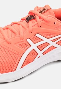 Baskets de sport corail avec une tige en mesh respirant, accents blancs et un design texturé. Elles disposent de lacets plats et d'une semelle blanche rembourrée.