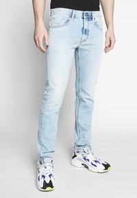 Ljust blå denimjeans med slim fit, femfickdesign och subtila blekningar. Matchas med vita och svarta sneakers med gröna detaljer.