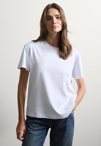 Camiseta blanca de algodón con cuello redondo y mangas cortas, combinada con jeans azules. Textura suave, corte relajado, diseño minimalista.