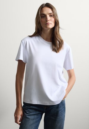 Weißes Baumwoll-T-Shirt mit Rundhalsausschnitt und kurzen Ärmeln, kombiniert mit blauen Jeans. Glatte Textur, lässige Passform, minimalistisches Design.