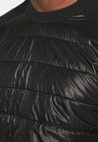 Czarna kurtka puchowa z pikowanym wzorem, eleganckim wykończeniem i prążkowanym dekoltem. Tkanina wydaje się gładka z delikatnym połyskiem.