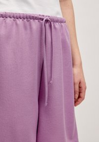 Lila sweatpants van een gestructureerde stof, met een elastische tailleband en een trekkoorddetail. De stof lijkt zacht en casual.