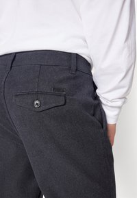 Tmavě šedé kalhoty ze směsi vlny mají zadní kapsu s knoflíkovým zapínáním a malou černou značkovou štítkem. Měkká textura a přizpůsobený střih.