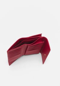 Červená kožená peněženka s texturovaným povrchem, několika sloty na karty a centrálním prostorem. Disponuje zapínáním na patent a minimalistickým designem.