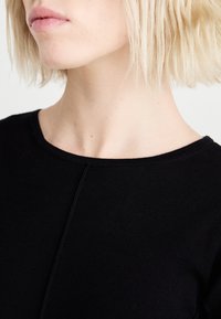 Black ribbed top featuring a round neckline and short sleeves, with a smooth texture and subtle seam detail along the front.