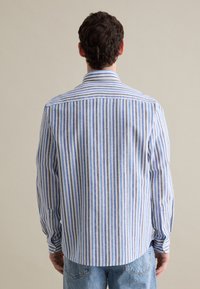 Camicia a maniche lunghe con strisce verticali blu e bianche, colletto button-down e orlo arrotondato. Realizzata in un tessuto leggero e testurizzato.