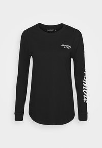 Zwart T-shirt met lange mouwen van katoen; heeft een wit logo op de borst en een tekstaccent op de linkermouw; afgeronde zoom.