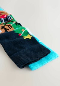 Nertiniai kojinai turi tamsiai mėlyną dizainą su elnio ir Kalėdų eglutės raštu, derinama su vientisomis šviesiai mėlynomis kojinėmis.