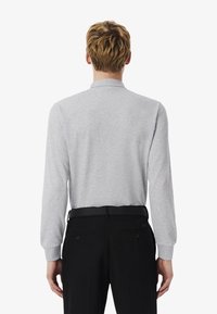 Långärmad grå pikétröja med krage. Tillverkad av mjuk tyg. Svarta byxor med sidofickor, med diskret logotyp på baksidan.