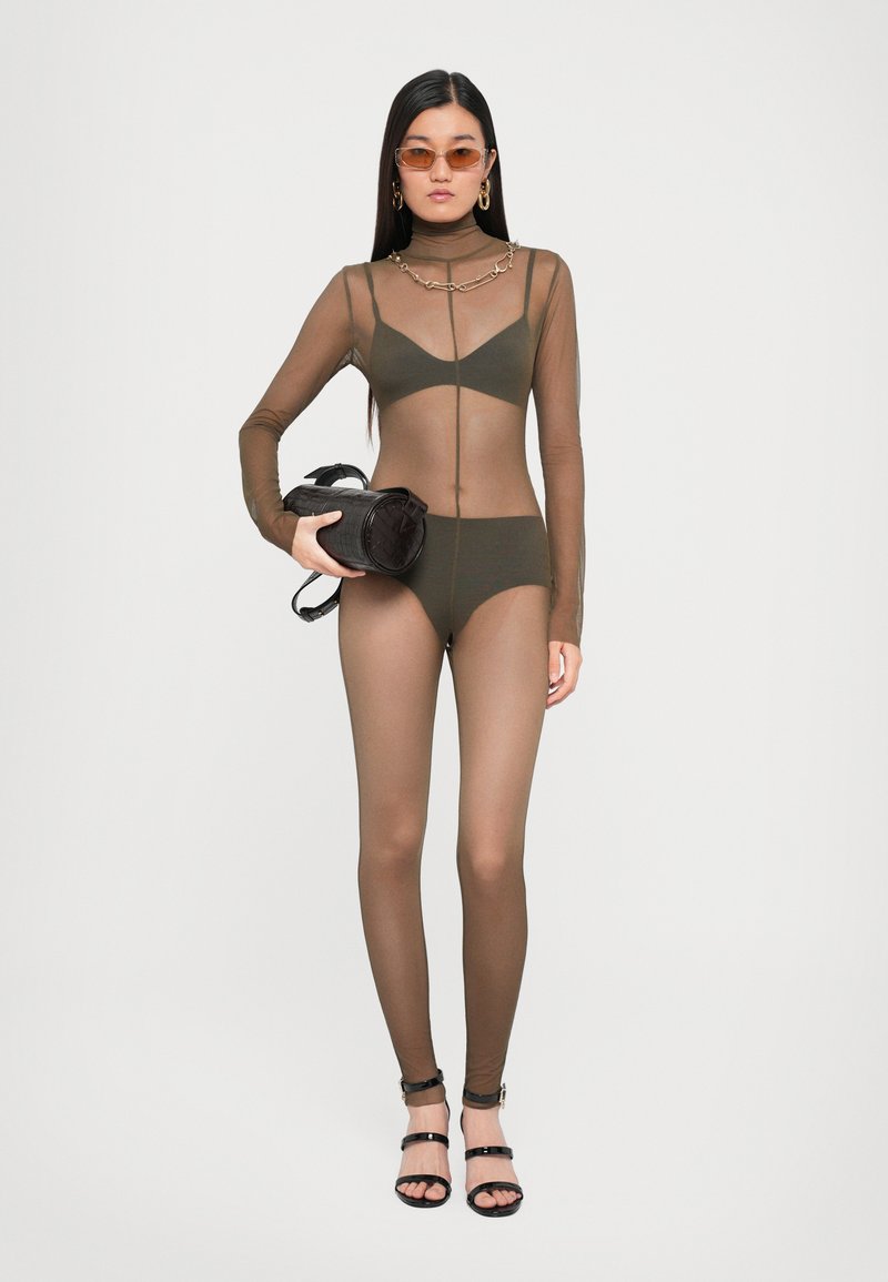 Olijfgroen mesh bodysuit met lange mouwen, hoge hals en kettingdetail. Model houdt een zwarte textuur handtas vast en draagt zwarte bandjeshakken.