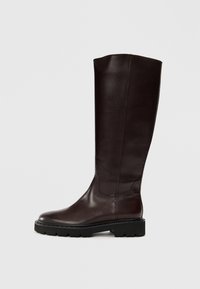 Bottes en cuir marron jusqu'aux genoux avec une finition lisse, un bout arrondi et une semelle en caoutchouc durable présentant une texture striée pour une meilleure adhérence.