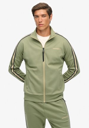 Giacca da tuta con zip verde con strisce nere e beige, caratterizzata da un colletto alto, chiusura con zip e logo sul petto. Tessuto dalla texture liscia.