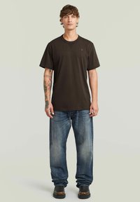 T-shirt corto a maniche corte marrone scuro con scollatura rotonda, indossato sopra jeans diritto blu sbiaditi e stivali in pelle nera.