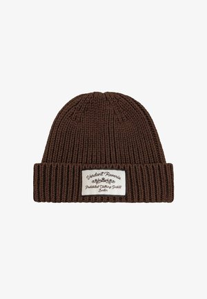 Rudas megztas kepurė su sulenkta briauna ir baltu stačiakampiu lipduku, pažymėtu "Verdant Reverie Prohibited Clothing GmbH Berlin."