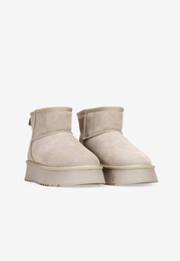 Stivaletti alla caviglia in suede beige con punta arrotondata, suola in gomma piatta e dettagli cuciti sulla cucitura. Altezza corta con design a risvolto.