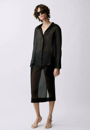 Schwarze durchsichtige Bluse mit Kragen, kombiniert mit einem passenden durchsichtigen Midirock. Das Outfit hat eine leichte, durchscheinende Textur.