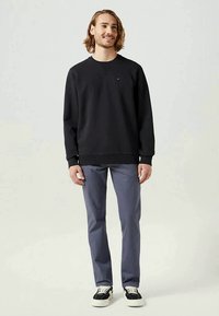 Sweater preto com decote redondo, punhos e bainha canelados; combinado com calças cinzentas e sapatilhas pretas com solas brancas.