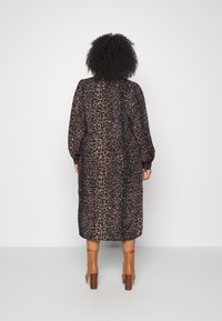 Robe à manches longues imprimée léopard en marron foncé et beige. Tissu doux, coupe longue jusqu'aux chevilles, poignets élastiqués, associée à des bottes à talons blocs beige.