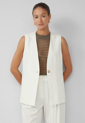 Wit mouwloos vest met een dubbelgeknoopte ontwerp en een enkele knop, gecombineerd met een getextureerde bruine gebreide top. Glad materiaal, getailleerde pasvorm.
