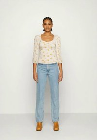 Top branco de manga bufante com padrão floral amarelo, combinado com jeans de perna reta azul claro e botas de salto bloco bege.