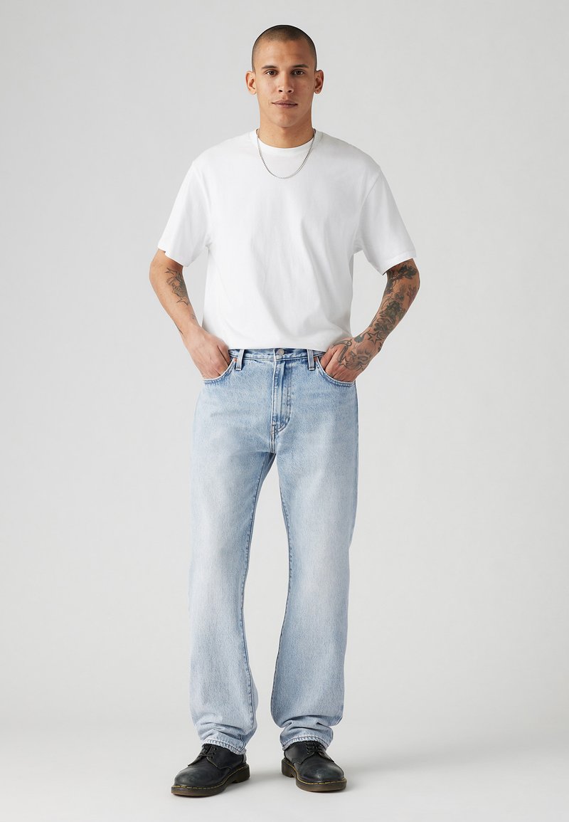 Witte katoenen t-shirt gecombineerd met lichtgewassen denim jeans, met rechte pasvorm, en zwarte veterschoenen. Eenvoudig ontwerp, strakke lijnen en geen patronen.