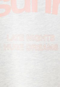 Texte sur tissu gris clair indiquant "LATE NIGHTS HUGE DREAMS" en lettres roses pâles contours.