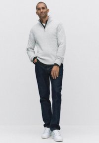 Ljust grå kabelstickad tröja med halvdragkedja, marinblå jeans och vita sneakers. Tröjan har ett strukturerat mönster och ribbade ärmslut.