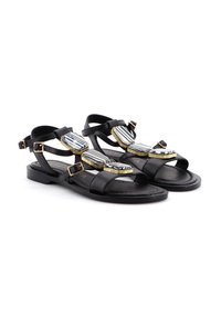 Sandali neri in pelle con suola piatta, caratterizzati da due decorativi accenti geometrici in oro e strisce nere/white, fissati con fibbie regolabili.