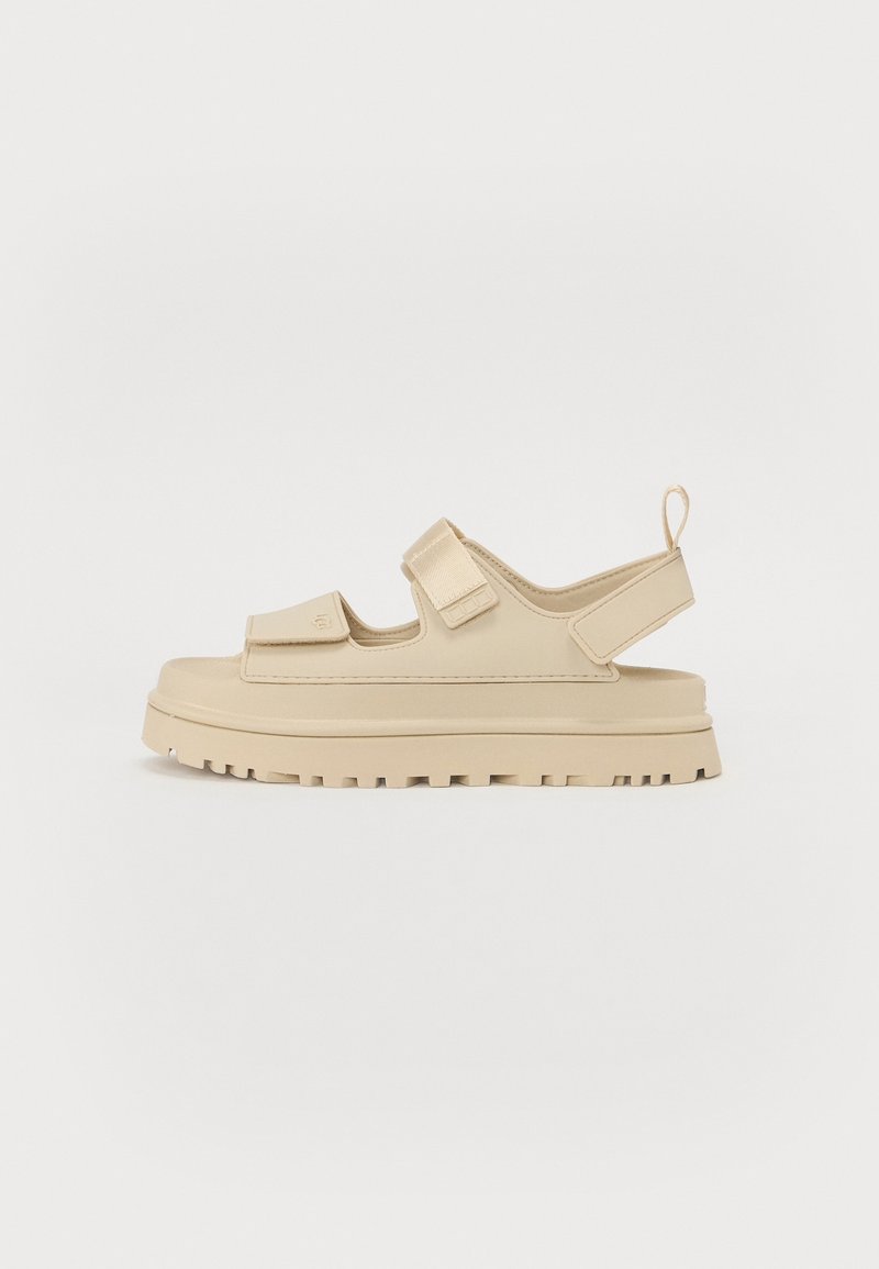 Sandale beige avec une semelle épaisse, deux brides réglables sur le pied et une bride au talon avec languette, présentée sur fond blanc.