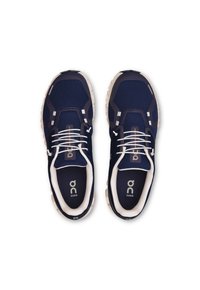 Baskets de course bleu marine avec tige en maille, lacets blancs et semelle couleur crème. Présente un logo et des accents de design hexagonal.