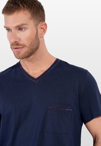 Marinblå V-ringad T-shirt tillverkad av mjukt tyg, med en bröstficka med färgad kant och en liten logodetalj nära fickan.