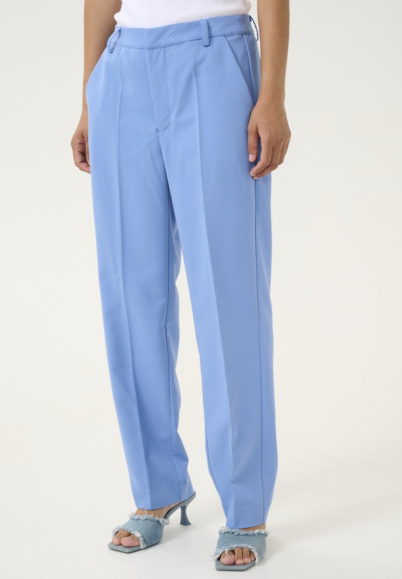 Pantalon bleu clair avec une coupe ajustée et un devant plissé. Le tissu semble lisse avec des poches latérales décoratives.