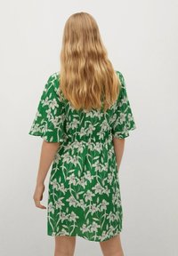 Grünes Blumenkleid mit kurzen Ärmeln, das eine taillierte Taille und ein Muster aus weißen Blumen auf gestreiftem Hintergrund zeigt.